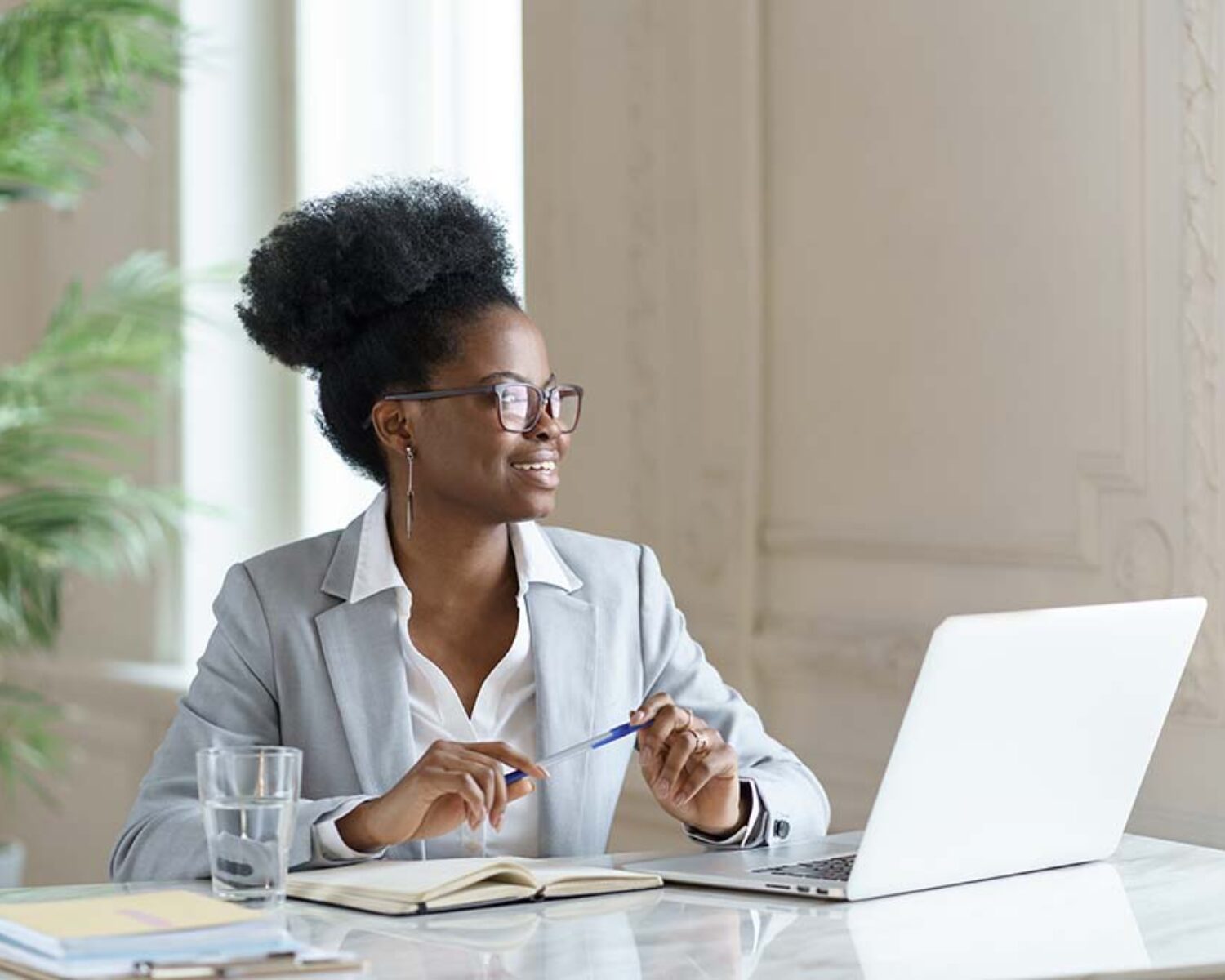 Smiling Afro woman in blazer wear glasses working at laptop computer at home office, dreaming about weekend vacation, looking away. Black girl student takes a break from work. Positive thinking